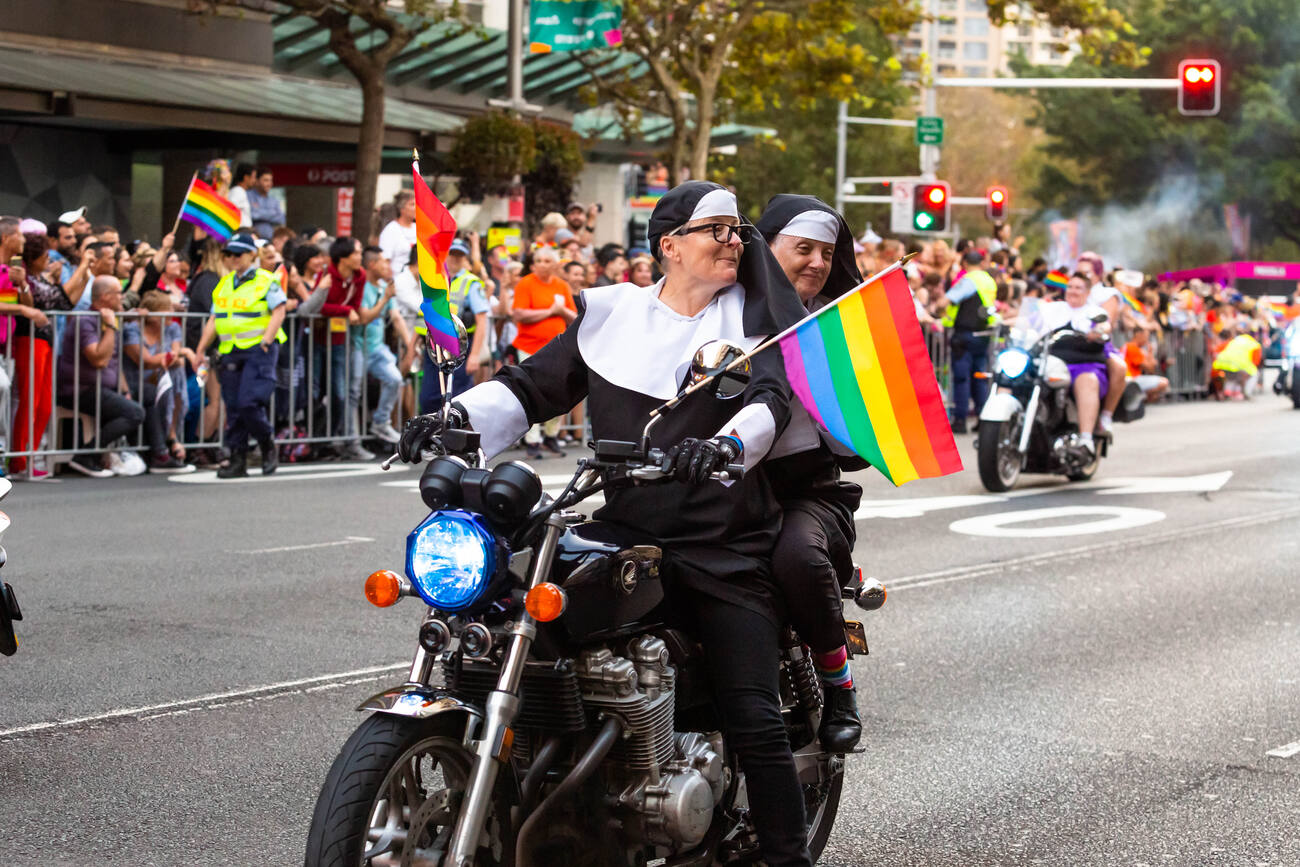 Nuns on a motorcycle flying a pride flag during a parade