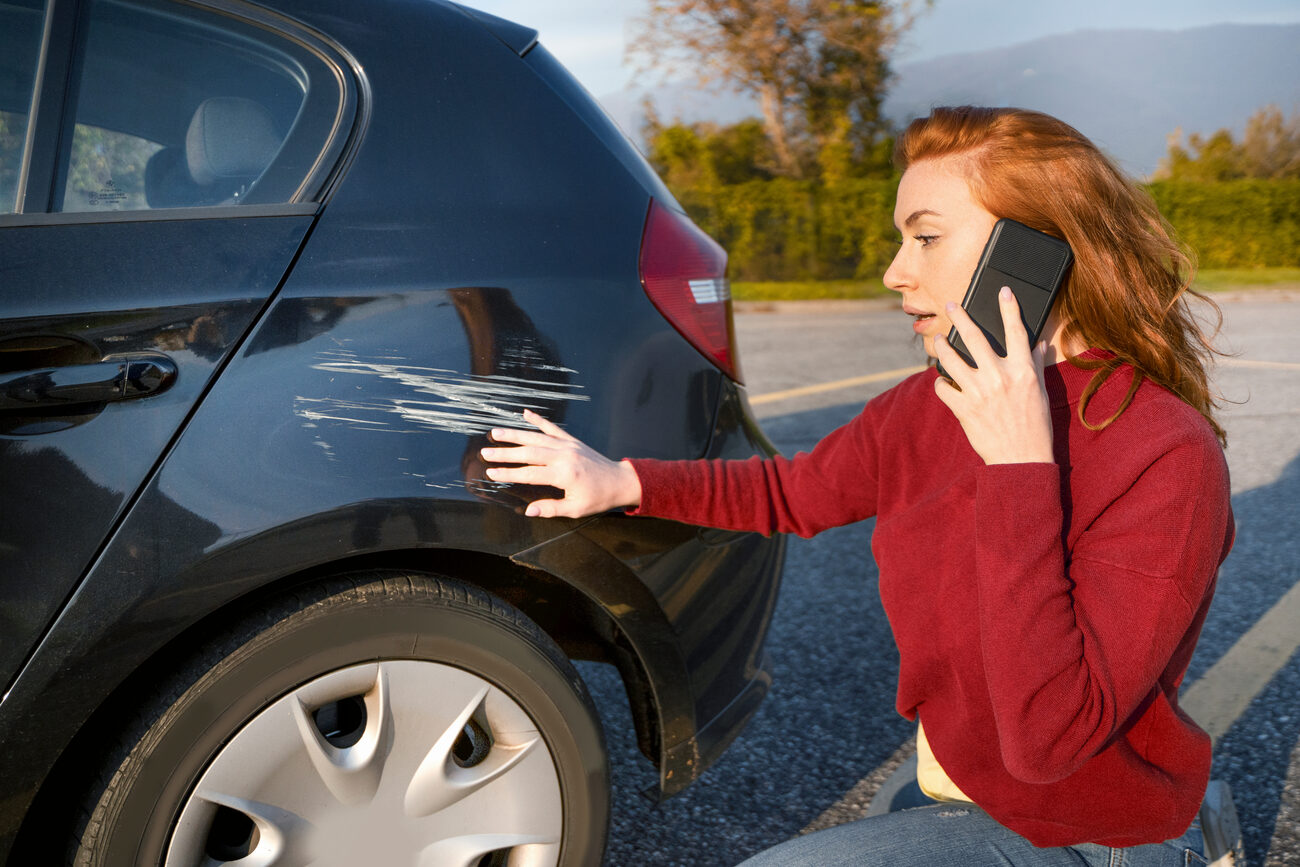 Person on the phone looking at scratches on their car