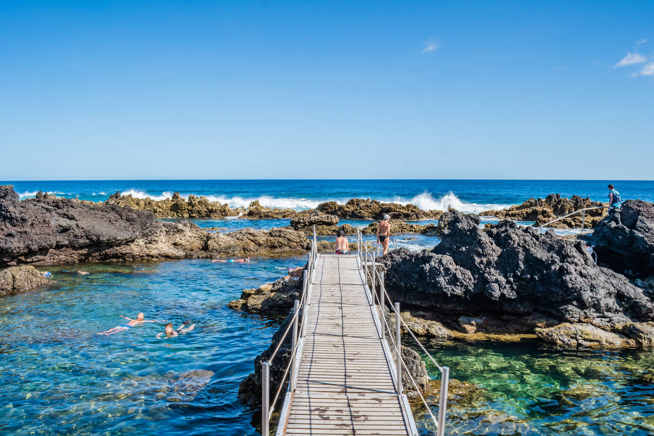 Rocky shore of the ocean with people floating in the water by a bridge