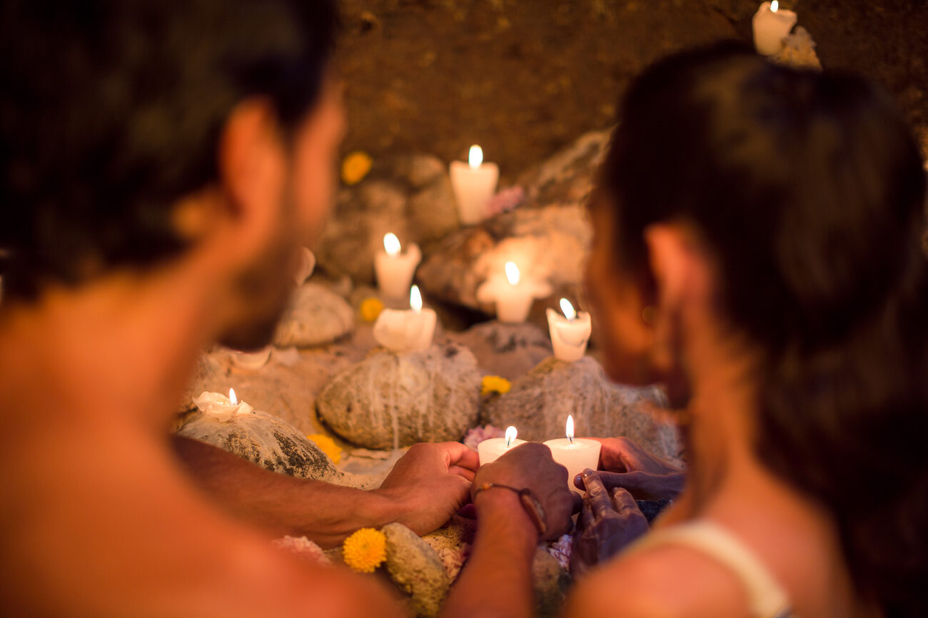 Hands holding lit candles in a cave