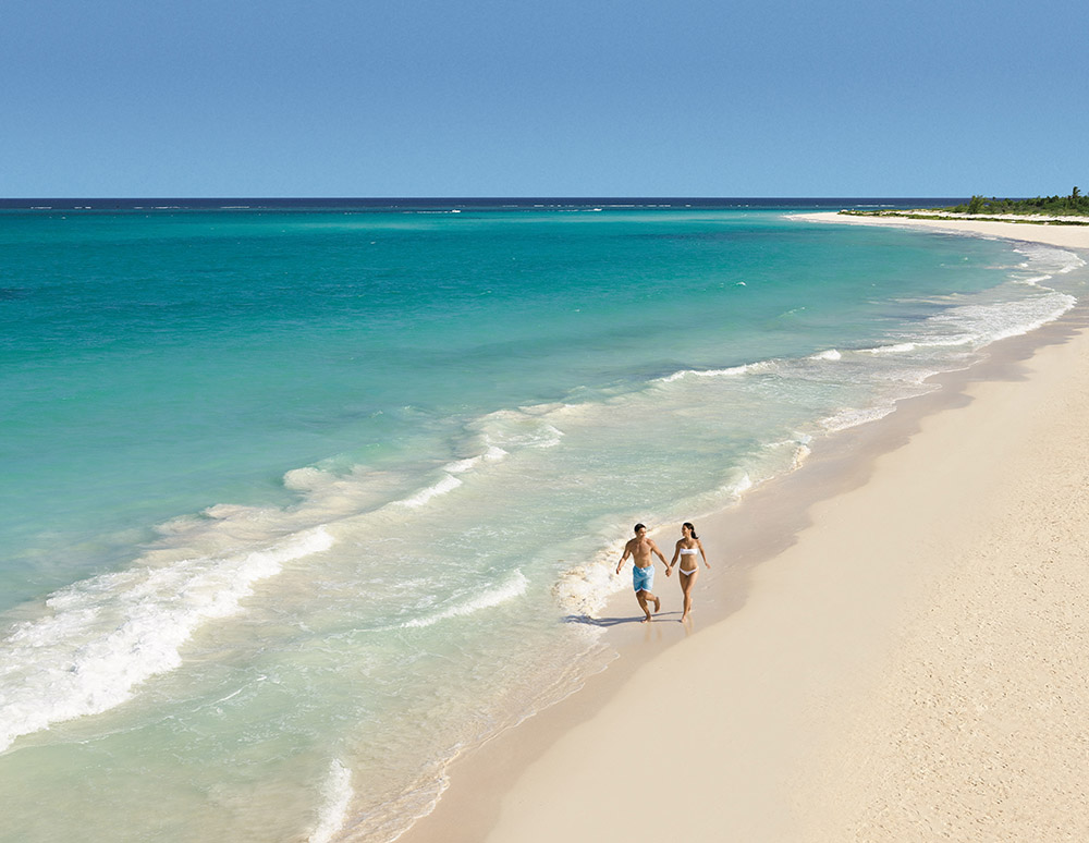 A man and a woman holding hands while running on the beach.