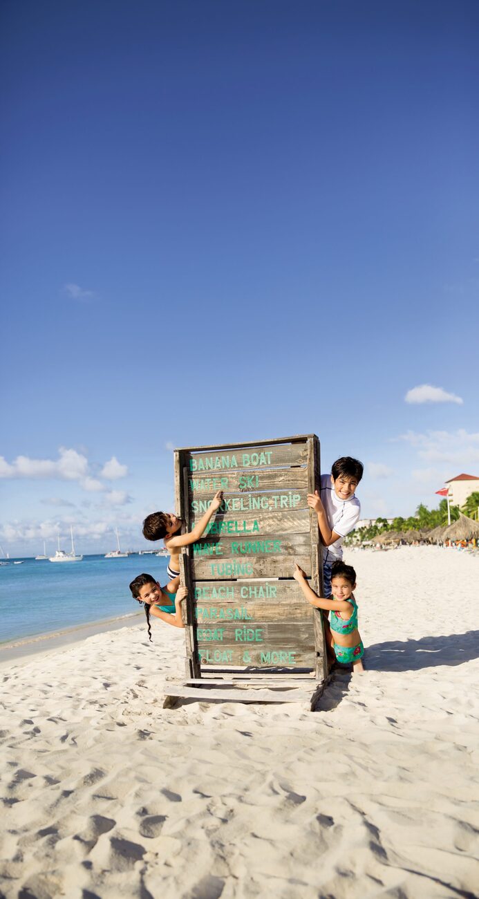 Kids on the beach pointing at a sign